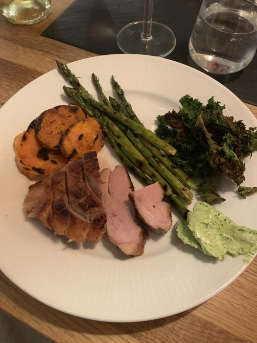 Tallrik med anka, grillad sparris, sötpotatis och sardellsmör, serverad med ett glas vit rioja.