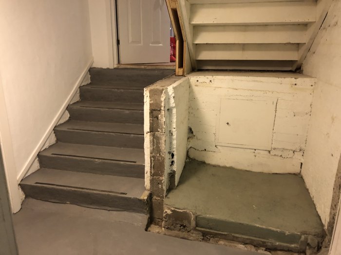 Ojämna leca-block i en källarhörna med trappa och betonggolv som behöver jämning.