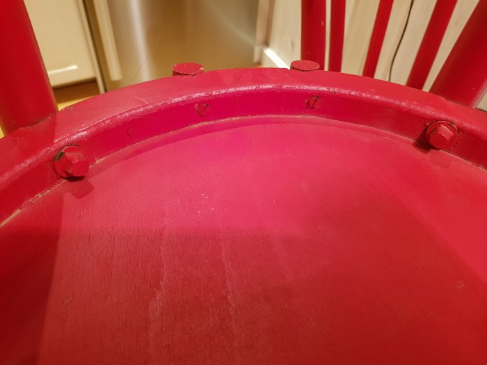 Närbild på detaljer av en röd Öglan köksstol med synliga skruv- och snickeridetaljer.