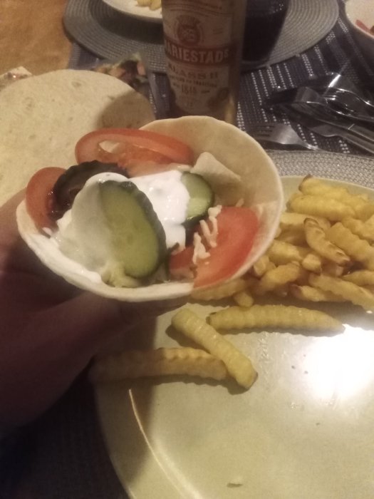 Tortilla med fyllning, crinkle-cut pommes frites och en ölflaska i bakgrunden.