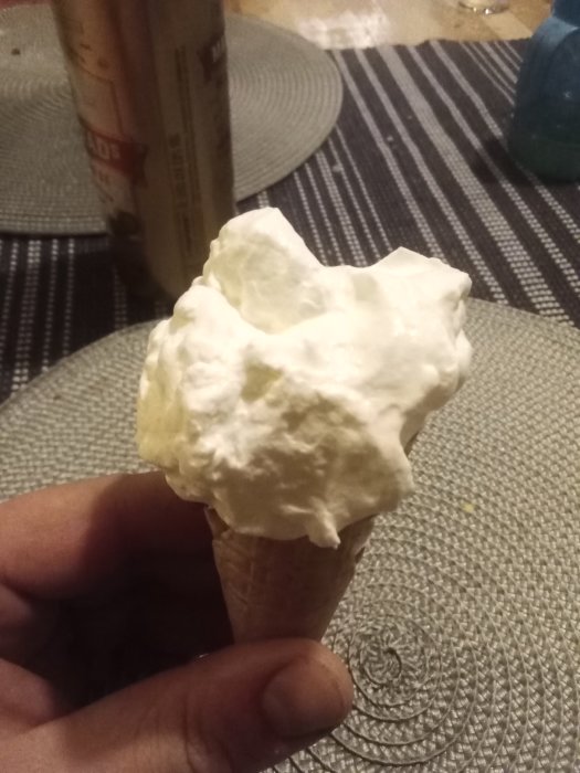 Hand som håller en strut med chokladpudding toppad med grädde.