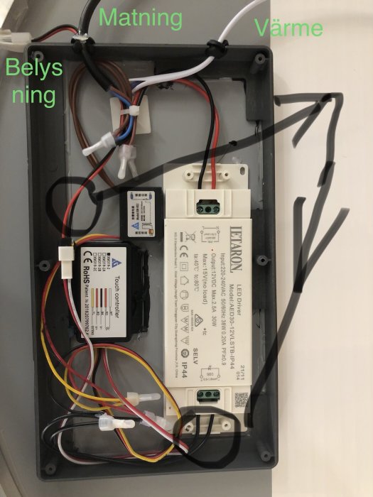 Baksidan av en spegel med elektriska komponenter, kablar och märkning för matning, belysning och värme.