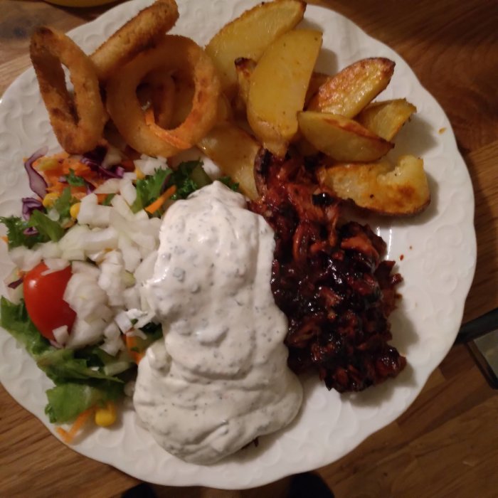 Tallrik med pulled pork, klyftpotatis, lökringar, grönsallad och örtagårdssås.