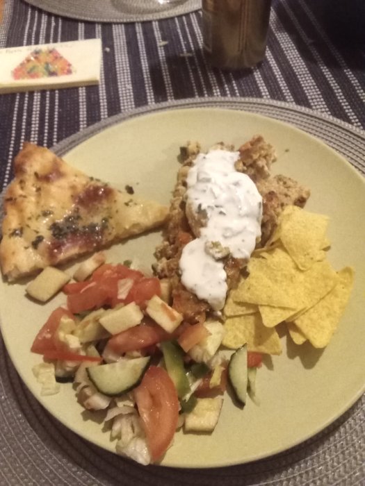 Tallrik med tacopaj, tsatsiki, hembakt bröd, sallad med avokado och nachochips.