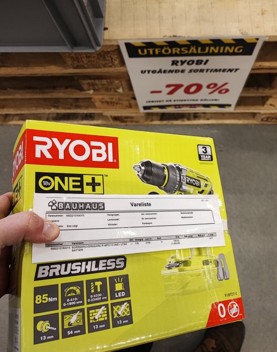 Hand håller en gul och svart RYOBI borrskruvdragare i förpackning framför en utförsäljningsskylt med -70% rabatt.