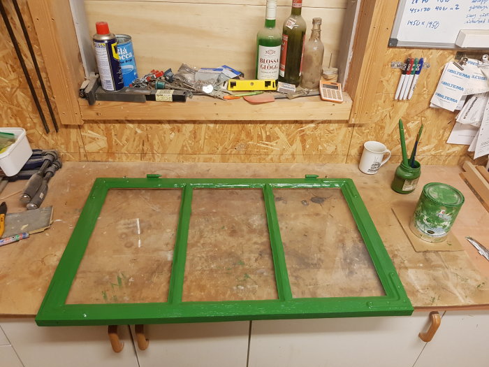 Nymålad grön fönsterbåge ligger på arbetsbänk med målarburk och verktyg runtomkring.