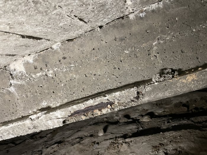 Skadad prefabricerad betongbalk i krypgrund med synlig rost och sprickor i betongen.