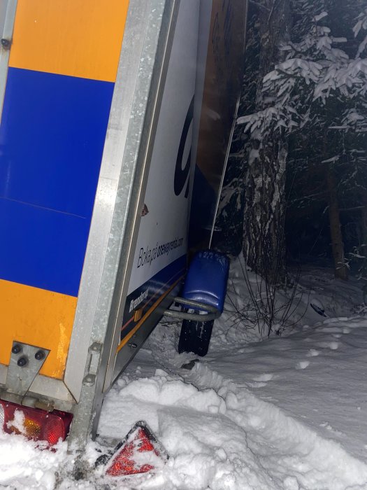 Släpvagn med högerbakhjul i diket, i snö, natten, med bakre delen nära marken.