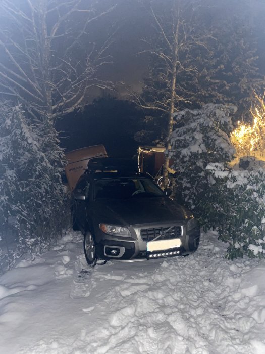 Bil fastnar med släp i snöigt dike på nattetid.