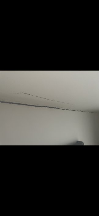 Stor spricka i vit takmålning som sträcker sig över taket, potentiellt sättningsskada.