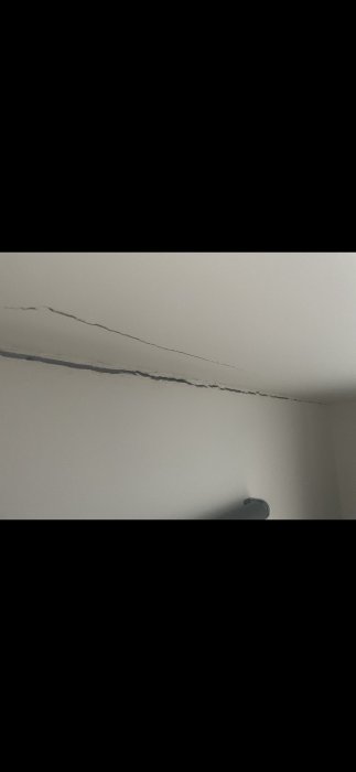 Stor spricka längs hörnet av en vitmålad vägg och tak vilket indikerar potentiella byggnadsskador.