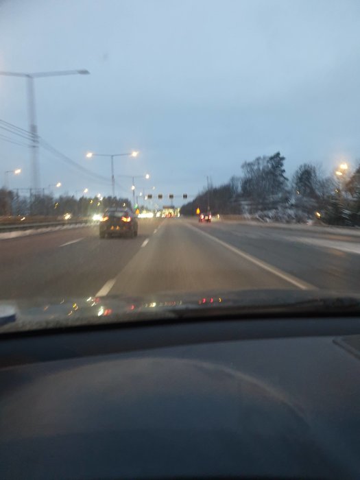 Bild från förarplatsen på en nästan tom motorväg med få bilar och gatlyktor i gryningen.