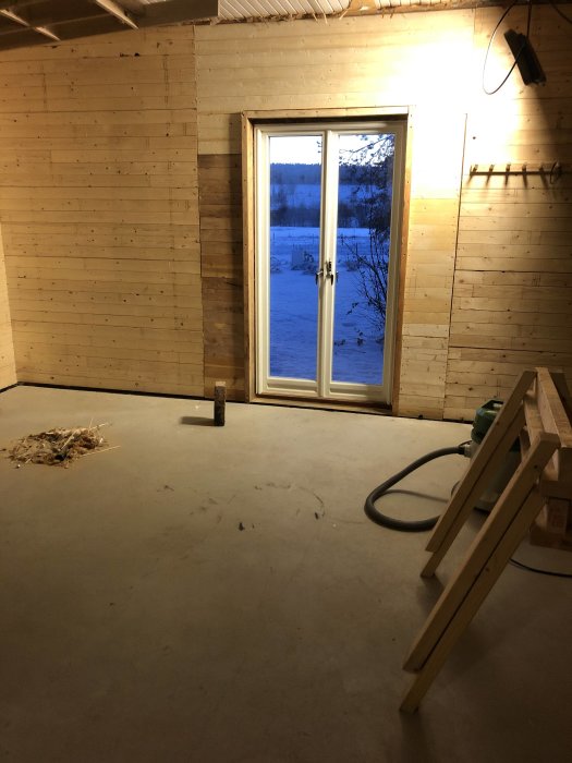 Innervägg med råspontskivor och fönster i ett renoveringsprojekt, med synlig isolering och ledningar.