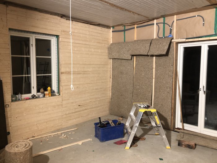 Renoverat rum med isolerade väggar, oskyddade reglar, stege och byggmaterial på golvet.