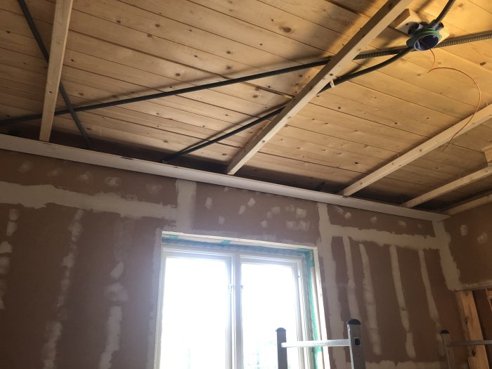 Renoverat rum under konstruktion med synliga träreglar i taket, oputsade väggar och elinstallationer.