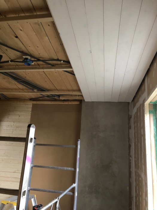 Renoveringsprojekt med vita slätspontstak och väggar i råspont och masonit under konstruktion med stege.