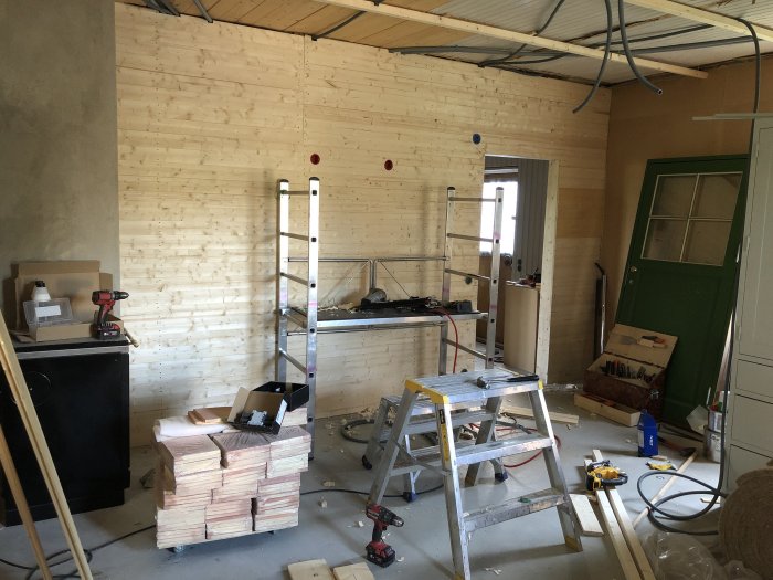 Renoveringsprojekt med råspontskivor på väggar, stege och byggmaterial i ett rum under konstruktion.
