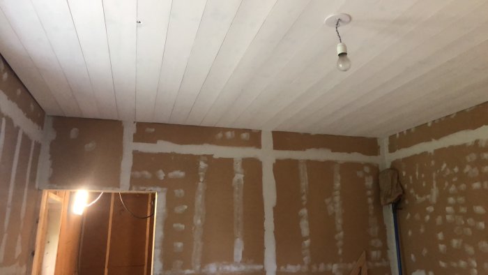 Renoverat rum med oisolerade väggar i spackel och vitmålade träreglar i taket.