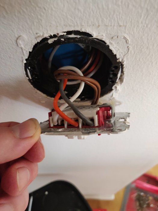 Elektriska kablar i en öppen väggkontakt som hålls av en hand under installationsarbete.