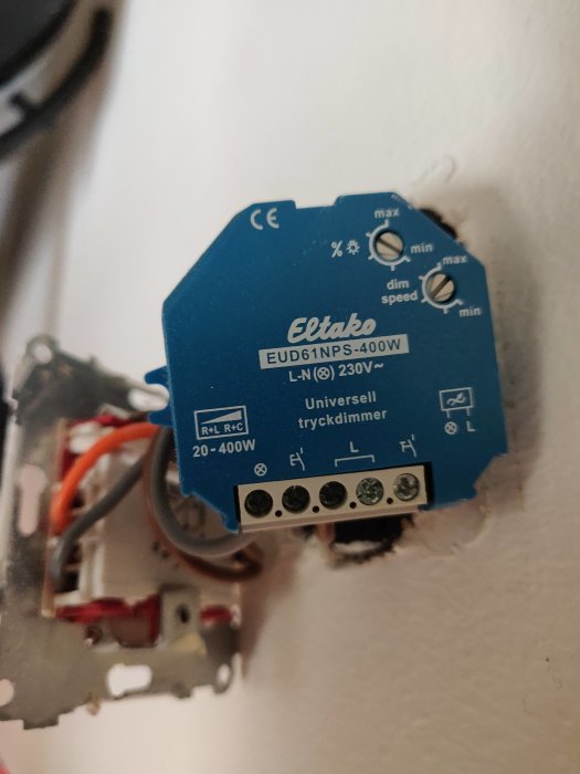 Eltako universell tryckdimmer EUD61NPS-400W installerad i vägg med synliga anslutningskablar och inställningsrattar.