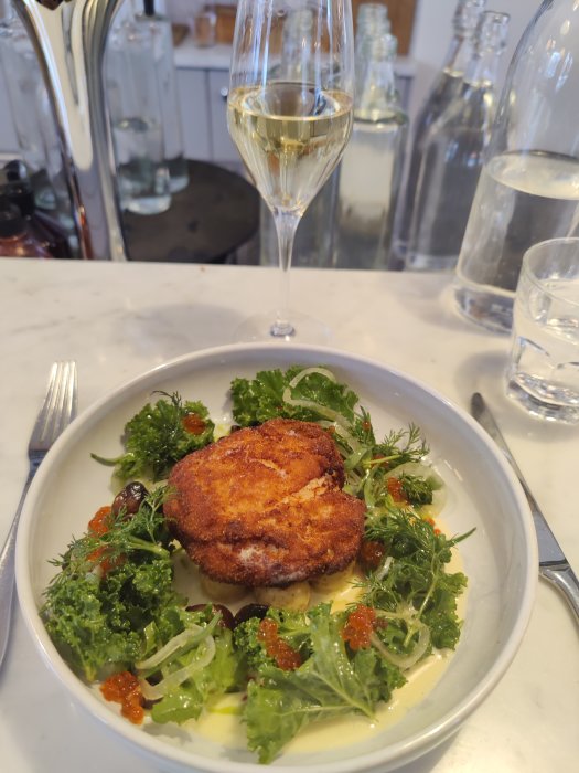 Wallenbergare med havssmak serverad med sallad, löjrom och ett glas vitt vin.