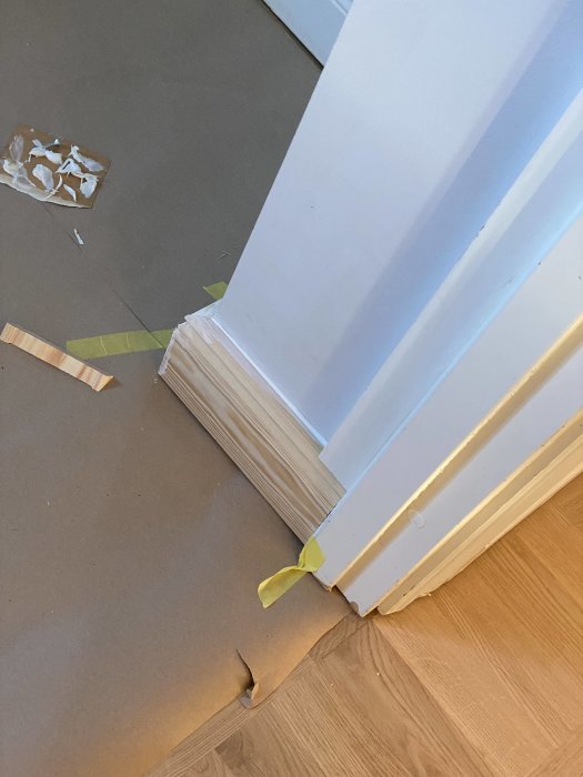 Lattialista ja ovenkarmi puuprojektissa, taustalla paperia ja teippiä valmisteluvaiheessa.