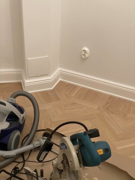 Saha ja pölynimuri puulattialla vastamaalatun valkoisen seinän vieressä. Seinällä on uusi valkoinen pistorasia.