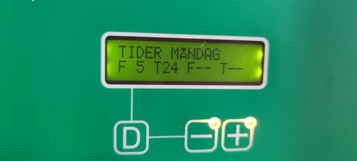 Display av värmepumpens styrpanel med texten "TIDER MÅNDAG F 5 T 24 F-- T--" och kontrollknappar.