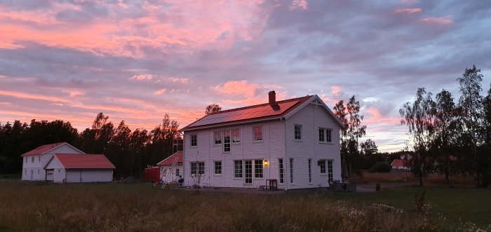 Villa med solceller på taket under en solnedgång med rosa himmel.