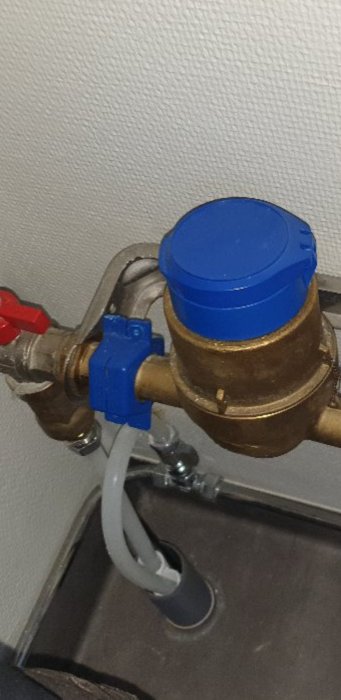 Vattenledning och värmekabel som passerar genom öppet grått plaströr i badrumsgolv.