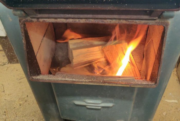 En eldstad med öppen lucka med brinnande vedstycken ovanpå vedträ.