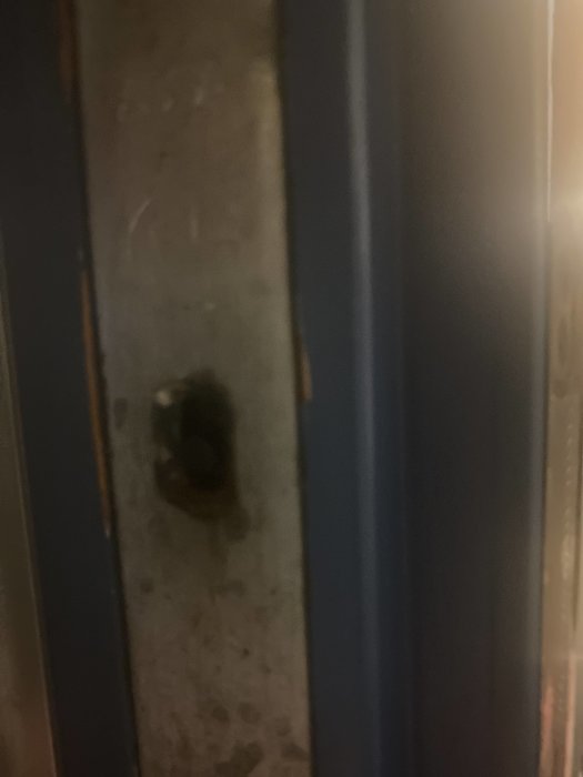 Lös svart låsknapp på sidan av en dörr, tecken på slitage och dålig funktion.