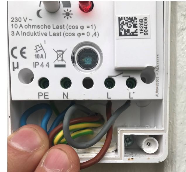 En hands håller en öppen elektrisk kapsling med trådar och anslutningar för en fjärrströmbrytare.