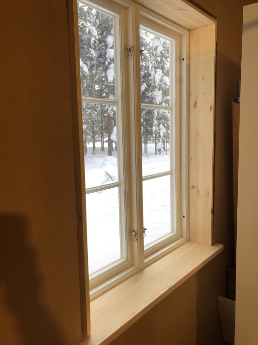 Träsalning och fönsterbräda av furu vid ett snöutsikt fönster, med eluttag integrerat i träpanelen.