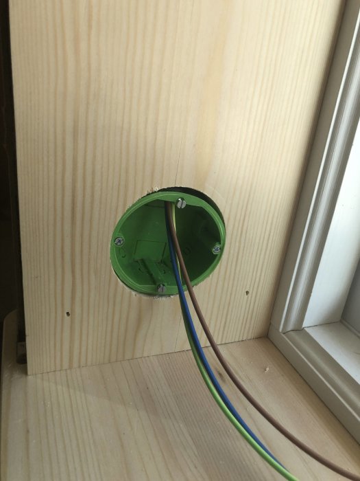 Uttag monterat i en fönstersalning av furu med elektriska kablar som sticker ut, bredvid ett vitt fönster.