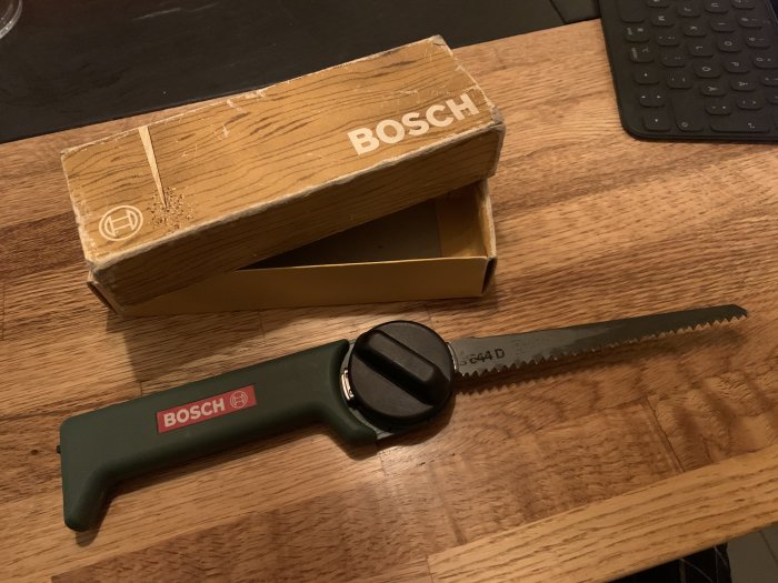 Manuell tigersåg från Bosch med sågblad framför en retroförpackning på träbord.