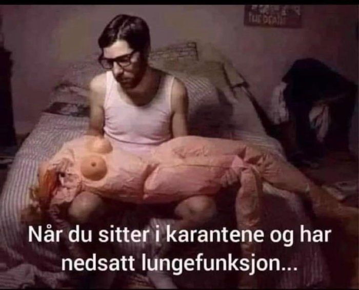 Man i linne sitter på en säng med en stor plyschlunga, humoristisk bild om karantän och lungfunktion.