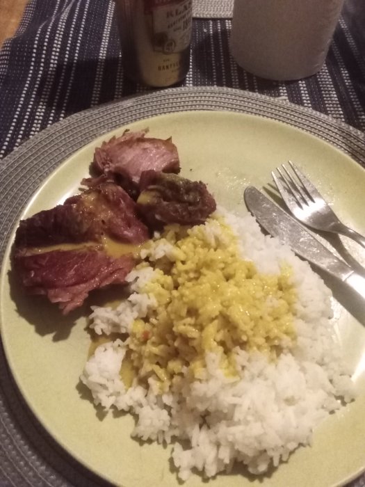 Tallrik med ris och currysås, fläsklägg vid sidan och en gaffel på tallriken, flaska i bakgrunden.