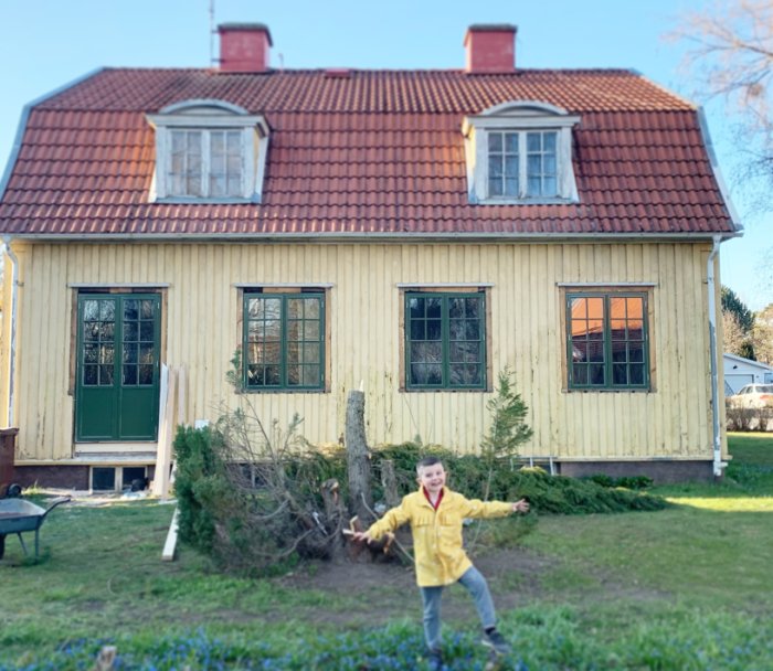 Ljust hus med röda takpannor och öppen altandörr under renovering, barn i gul jacka framför.