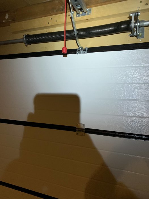 Garageports interiör med ett löst fäste på övre dörrbladet, skenor ovanför och en fjädermekanism.