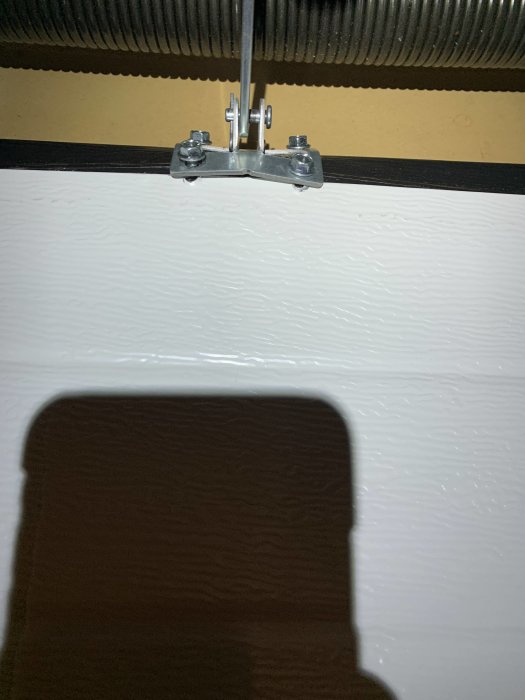 Befästningsdetaljer för en garageports automatiska öppnare med fokusering på övre dörrbladets fäste och skenorna.