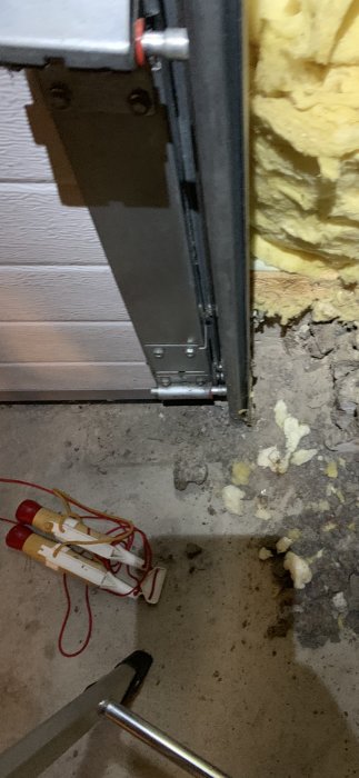 Garageportens underkant med synlig isolering och en del av portens mekanism, bredvid ligger verktyg på ett betonggolv.