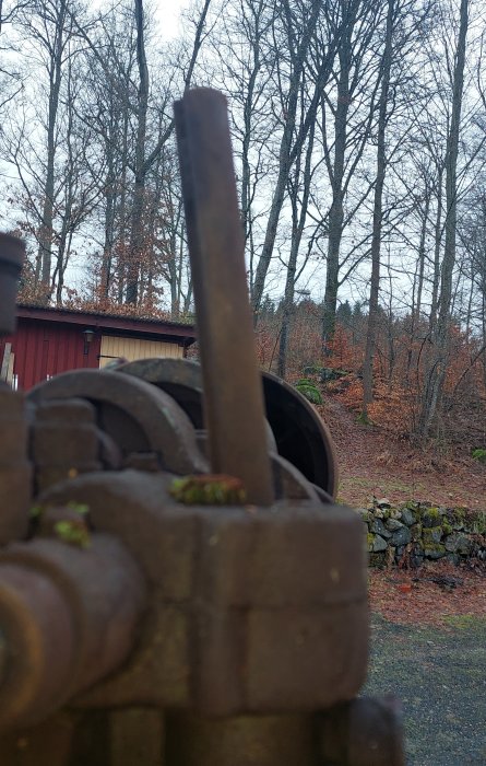 Krökt axel på en Segic pelarborr med bakgrund av träd och röd byggnad.