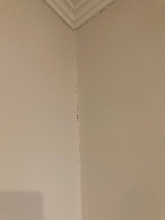 Sprickbildning i ett hörn där vägg och taklist möts i ett äldre hus, indikerar möjlig rörelse eller skadeorsak.