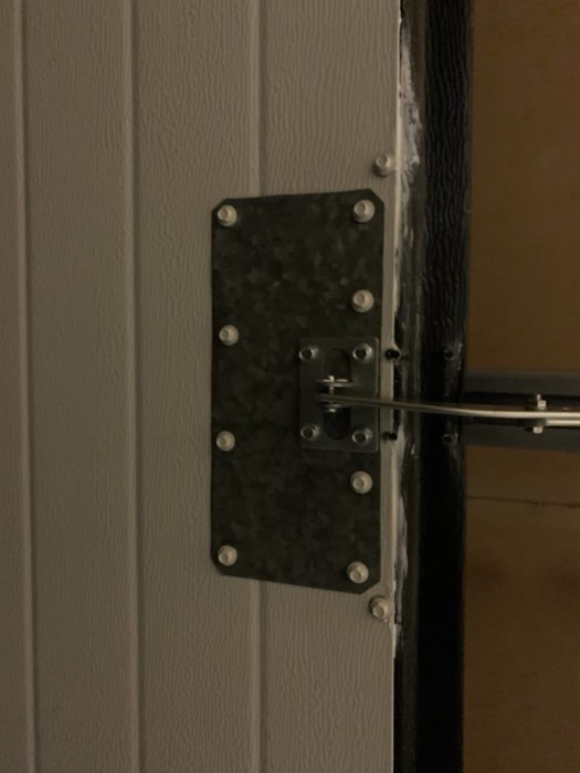 Stabiliserande fästplatta för portmekanism monterad på vit garageportspanel.