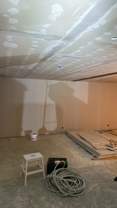 Spacklat tak med oslipade gipsskivor, kablar och arbetsmaterial syns i ett rum under renovering.
