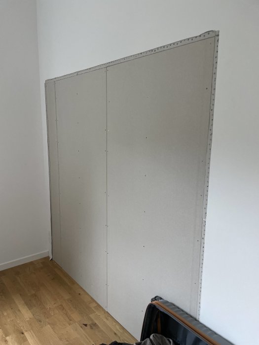 Ny uppförd gipsvägg i hörn av rum som förberedelse för walk-in closet, ommålad, parkettgolv synligt.