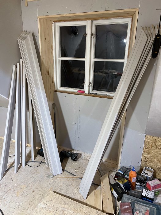 Nymålade foder i grön umbra staplade i ett renoveringsrum med fönster och verktyg på golvet.