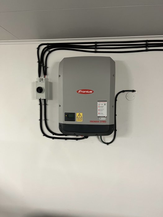 Fronius Symo solinverter installerad på vit vägg med ordnad kabeldragning.