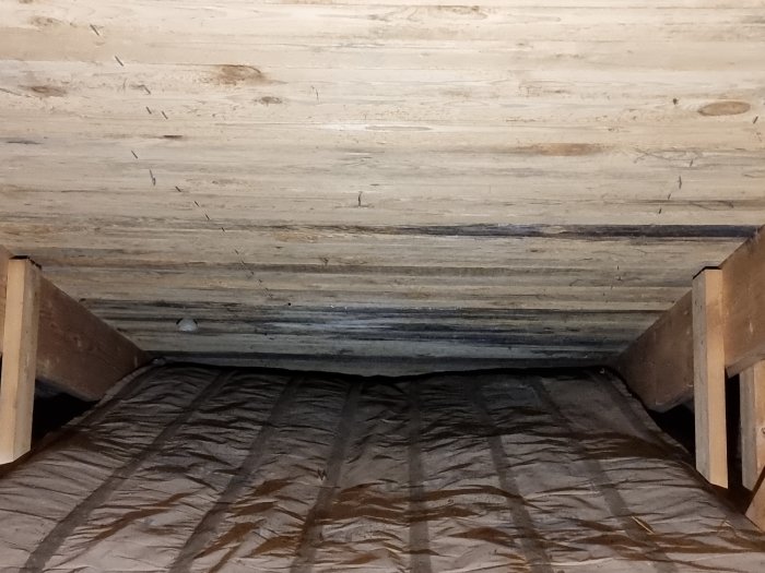 Mörkfärgat råspont på vind med isolering under, brist på luftspalt synlig.